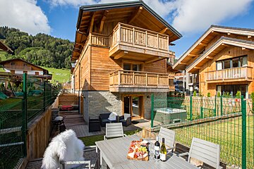 A bottle of wine sits on a table in front of a wooden house