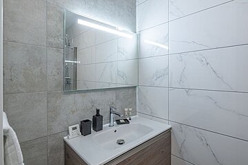 A bathroom with marble tiles and a sink and mirror