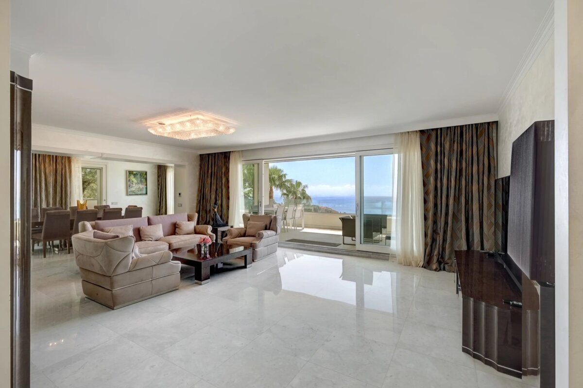 Elegant living room with plush sofas, glossy white floors, and an incredible ocean view through expansive glass doors.