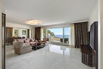An elegant, spacious living room with plush sofas, polished tile floors, and large glass doors opening to a scenic ocean-view terrace.