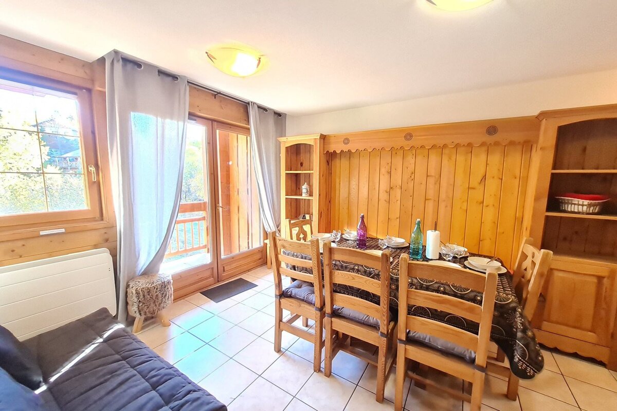 A rustic dining room with a wooden table set for a meal, wood-paneled walls, and a large window/balcony door.