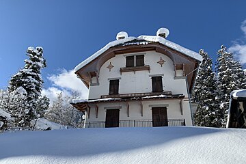 A large white house with a balcony and mountains in the background