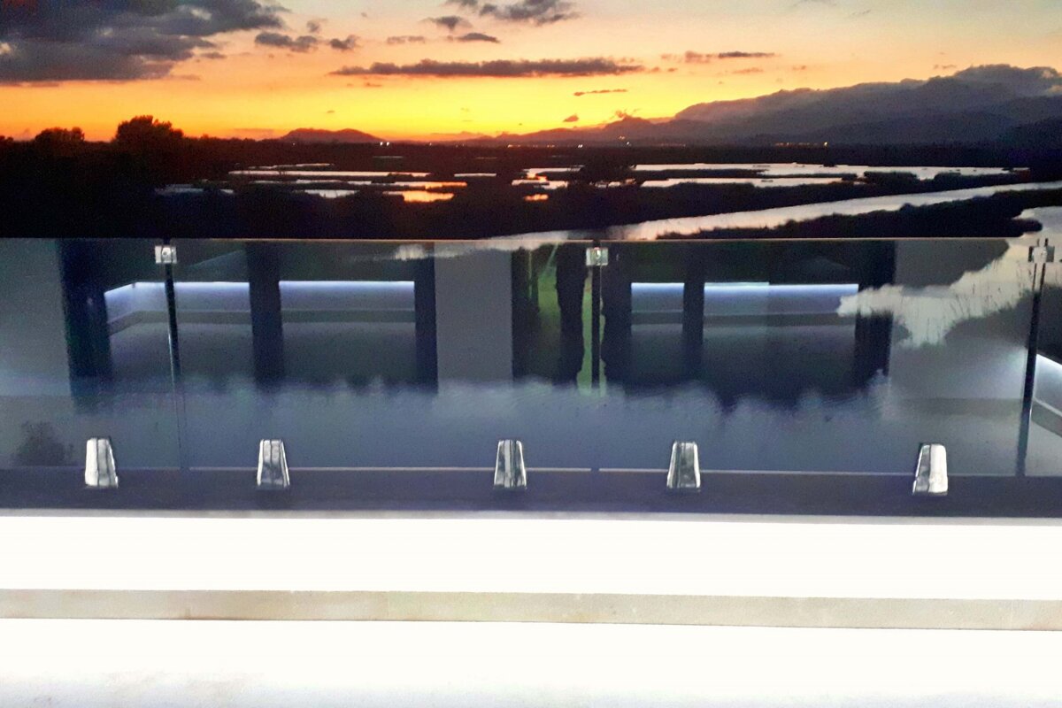 A sunset over a body of water is reflected in a glass railing