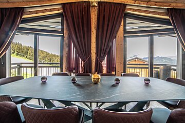 Elegant dining room with a large table and panoramic views of a forested mountain landscape through floor-to-ceiling windows.
