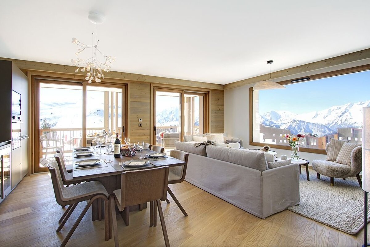 Modern chalet living-dining room with a set table, cozy seating, and breathtaking panoramic views of snow-covered mountains.