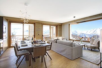 Modern chalet living-dining room with a set table, cozy seating, and breathtaking panoramic views of snow-covered mountains.