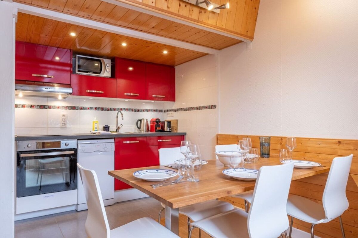 A kitchen with red cabinets and white chairs and a table with plates and glasses on it