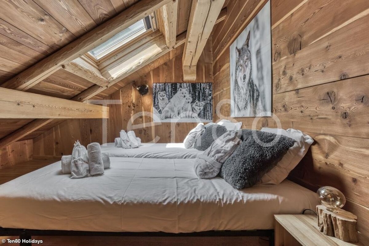 A cozy wooden attic bedroom with a skylight, two single beds, and wolf artwork on the walls.