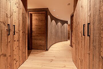 A modern rustic hallway with warm wood-paneled doors, wardrobes, light timber floors, and a curving, textured wallpapered wall.