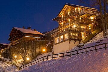 Cozy, warmly lit wooden chalets on a snowy alpine hillside at night.