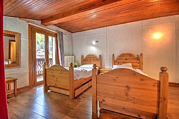 Cozy room with two wooden beds, a rustic wooden ceiling and floor, and a door opening to a balcony.