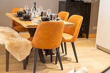 Modern dining area featuring a wooden table set for a meal, orange upholstered chairs, and a bench with a furry throw.