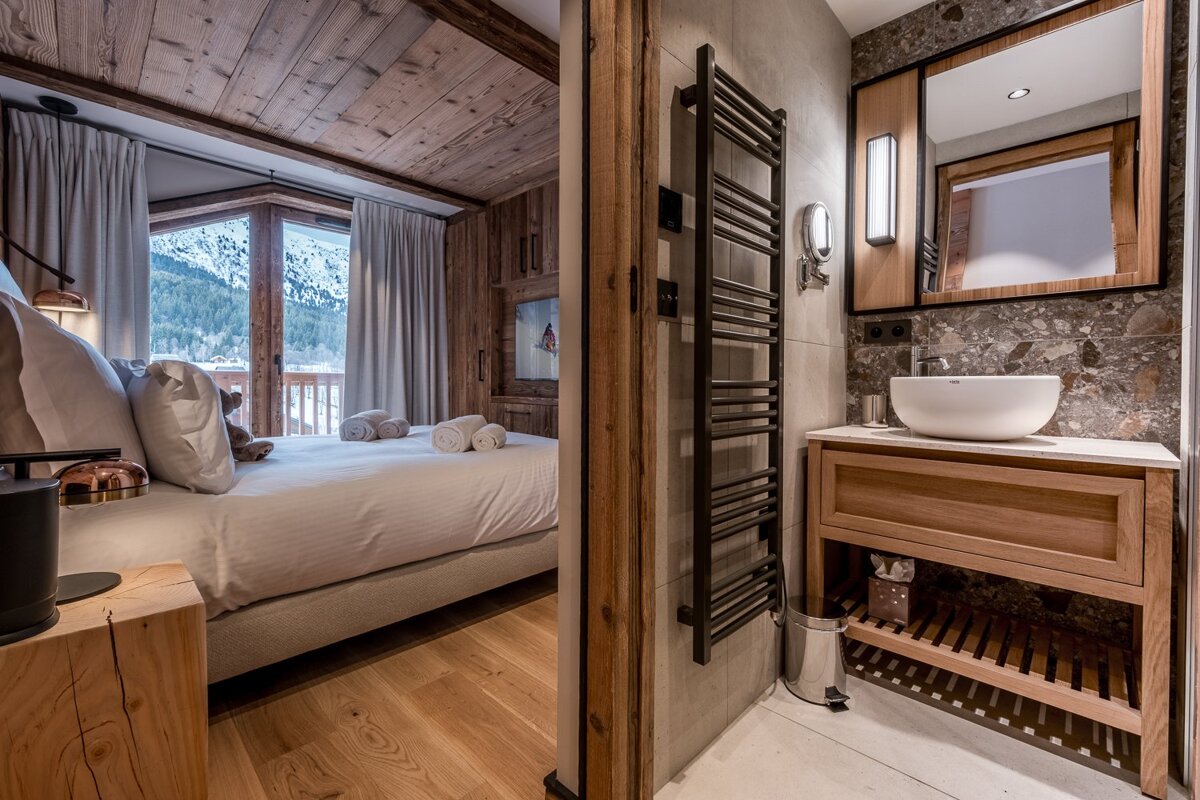 A cozy chalet bedroom with a snowy mountain view, connected to a chic bathroom featuring wood, stone, and a modern vessel sink.