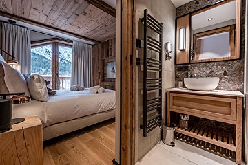 Rustic wood-paneled bedroom overlooking snowy mountains, connected to a chic bathroom with a modern vessel sink, wooden vanity, and towel warmer.