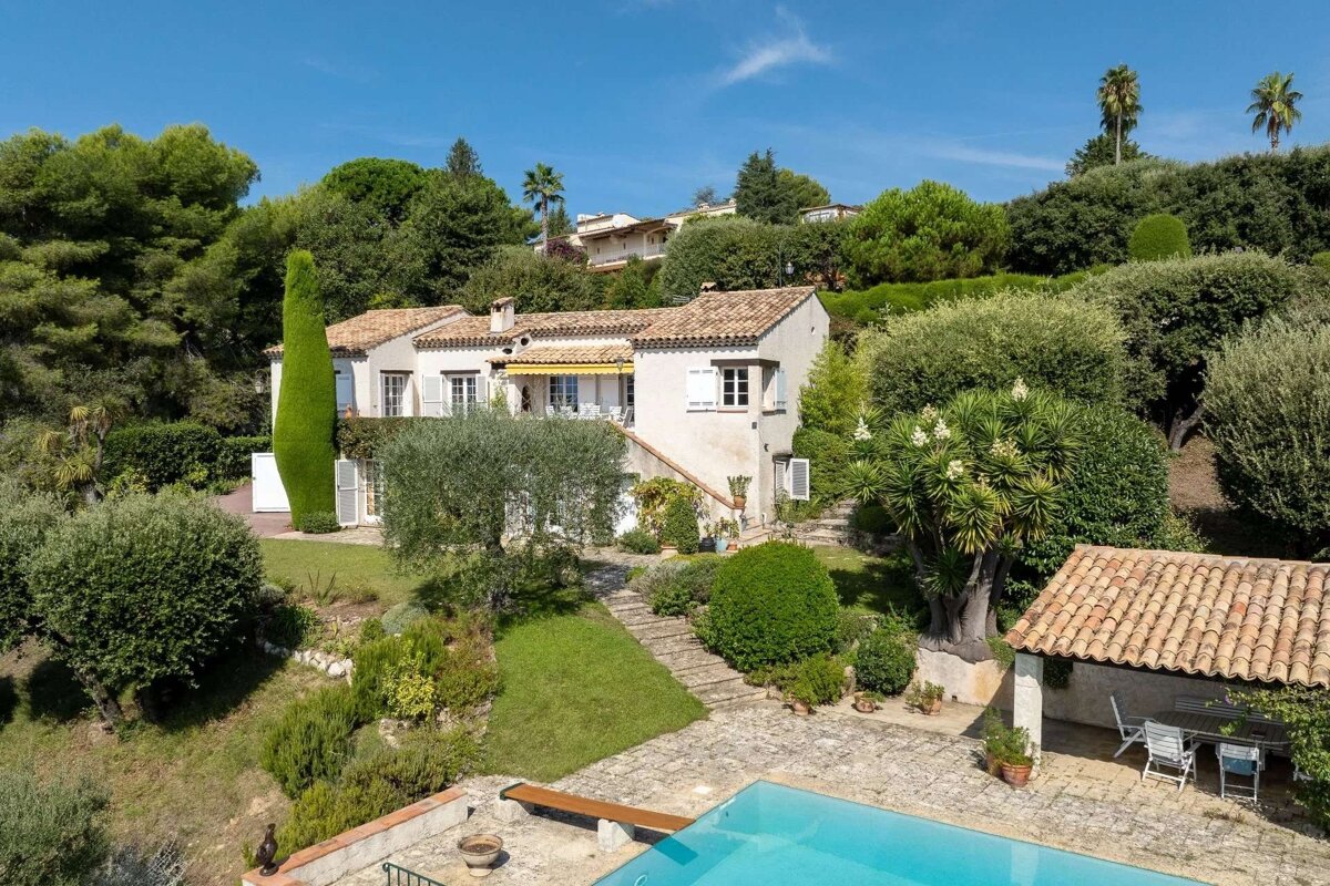 A charming Mediterranean-style villa with terraced gardens, a pool, and lush greenery under a clear blue sky.