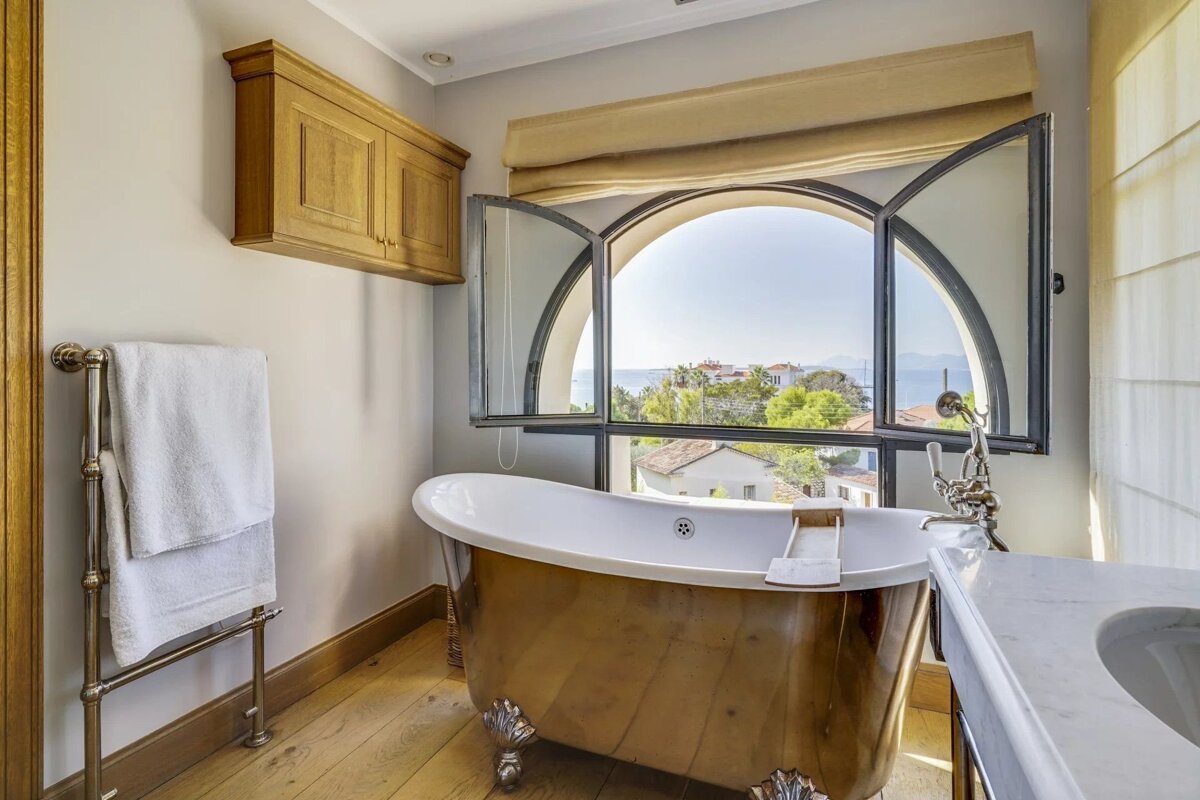 A luxurious bathroom featuring a gold clawfoot tub by an open arched window with a beautiful ocean view.