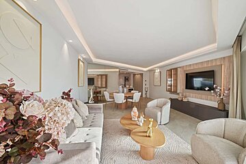 A chic, open-plan living and dining space with contemporary furniture, subtle lighting, warm neutral colors, and an elegant floral display.