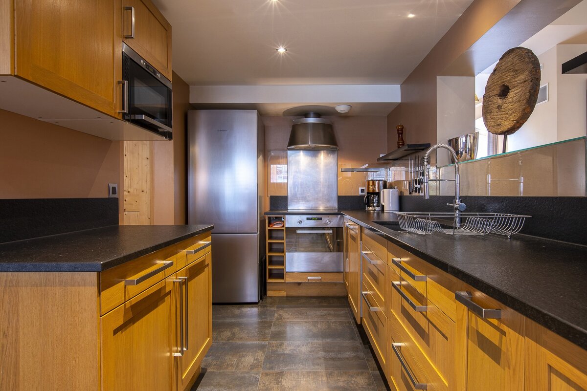 A modern kitchen featuring wooden cabinets, black countertops, and stainless steel appliances.