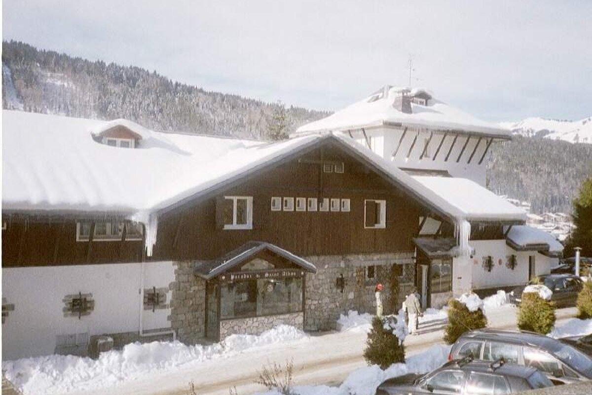 A cozy, snow-covered alpine lodge with icicles and cars parked outside, set against a winter mountain landscape.