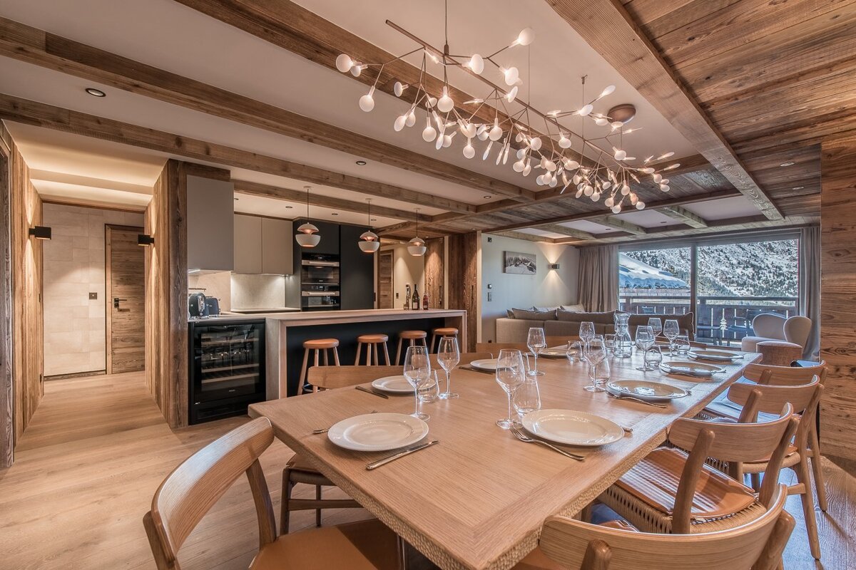 Luxurious alpine dining room with wood paneling, a large set table, a modern branch chandelier, and a snowy mountain view.