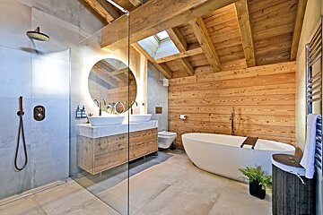 Modern rustic bathroom with wood paneling, a freestanding tub, a double vanity with a backlit mirror, and a glass-walled shower.