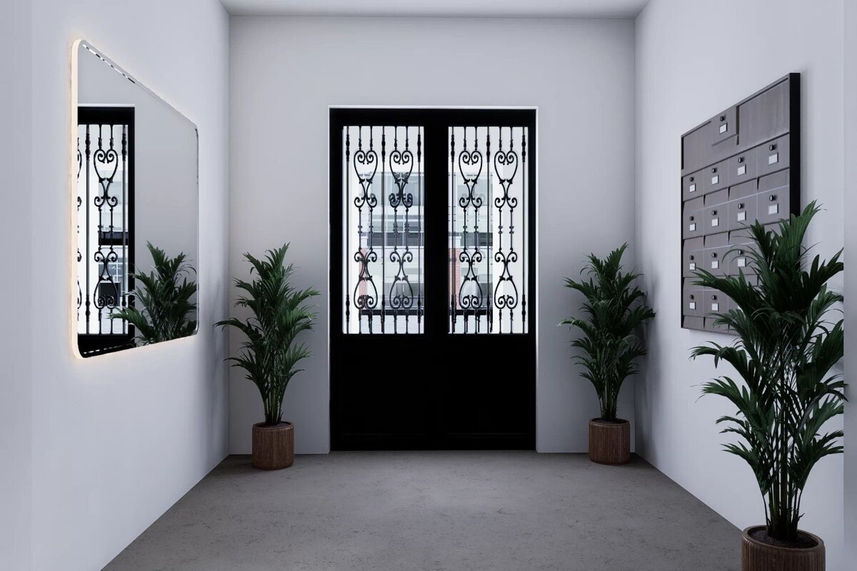 A modern hallway with white walls, a black double door, potted plants, a large mirror, and mailboxes.