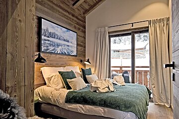 Cozy rustic bedroom with wood-paneled walls, a green throw, and glass sliding doors opening to a snowy winter view.