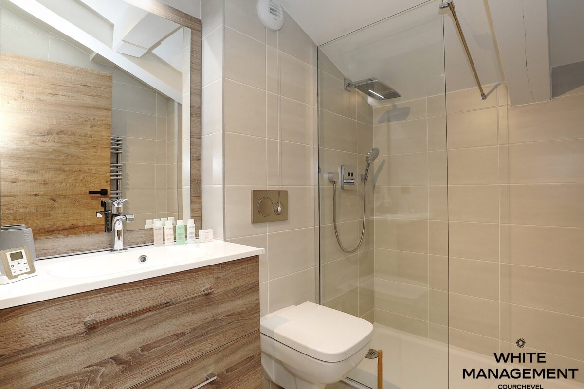 A modern bathroom featuring light beige tiles, a wooden vanity with a sink and mirror, a toilet, and a glass-enclosed walk-in shower.