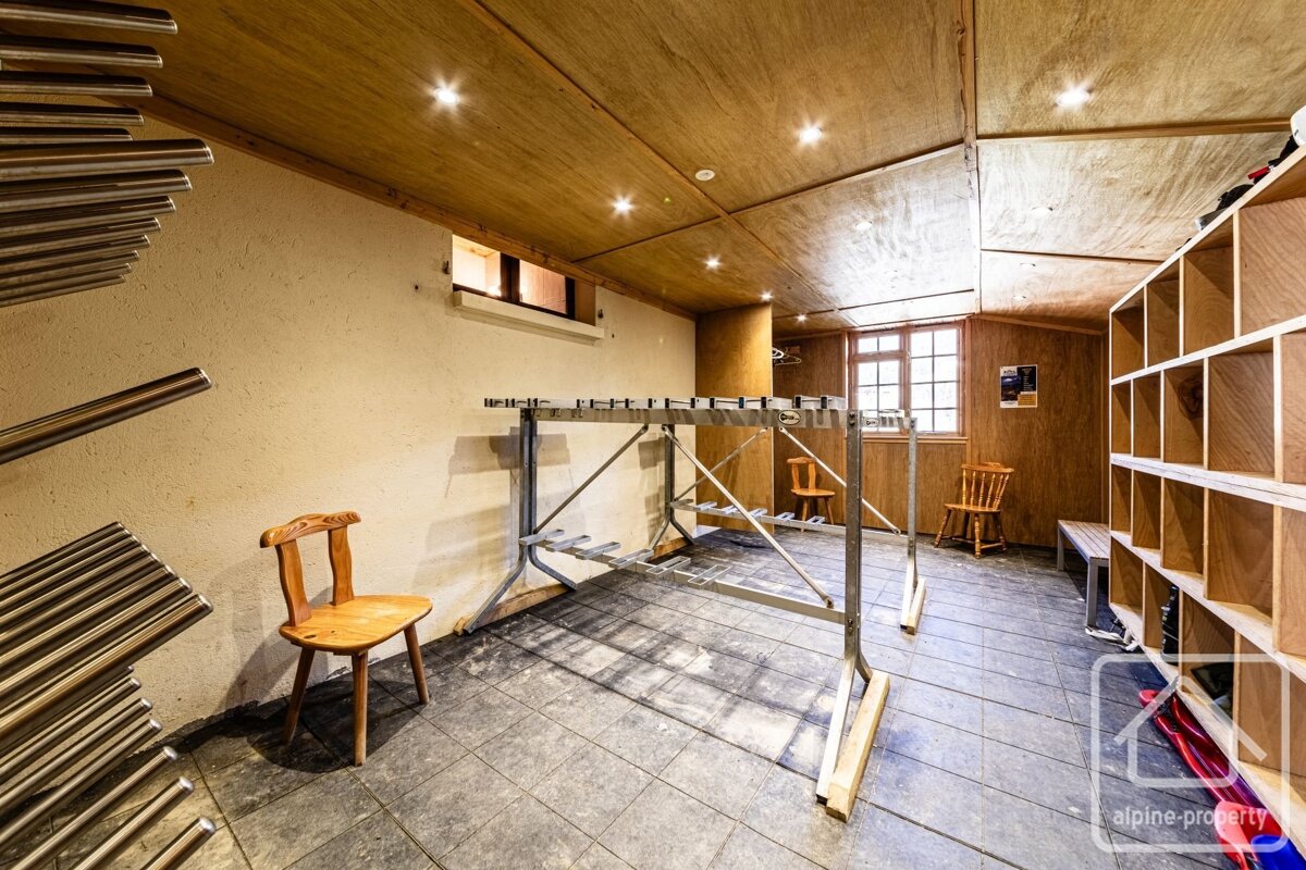 An empty ski room with a central boot drying rack, wooden cubbies, paneled walls/ceiling, tiled floor, and small windows.