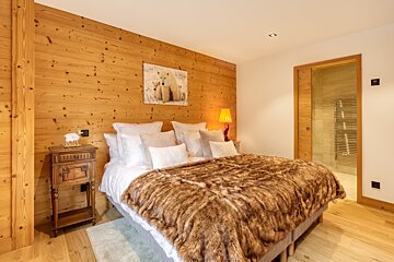 A cozy alpine bedroom with a wood-paneled wall, a bed covered in a plush faux-fur blanket, and a polar bear picture.