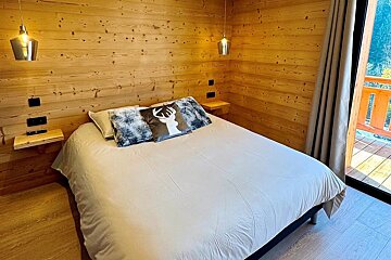Rustic wood-paneled bedroom with a comfy bed, deer pillow, and a balcony view.