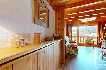 Cozy, wood-filled chalet interior featuring a rustic mirror, leading to a balcony with a scenic mountain and valley view.
