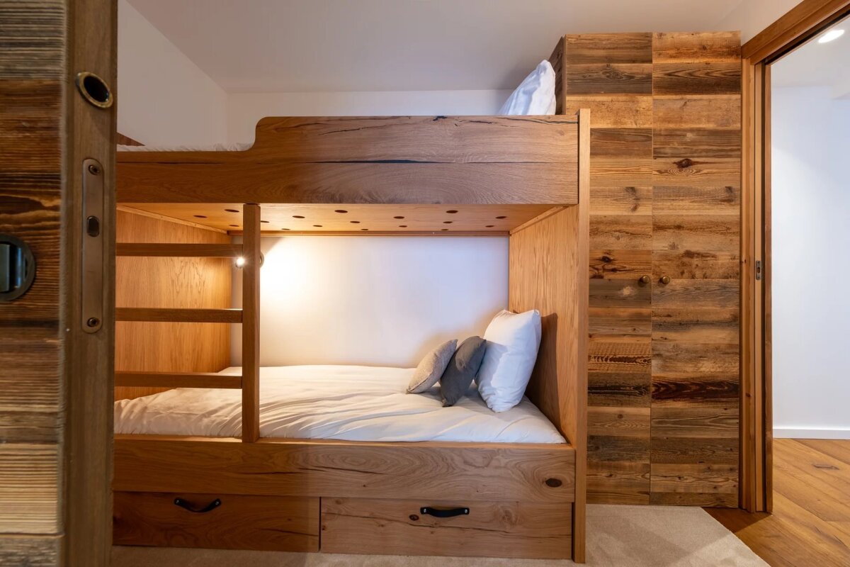 Rustic modern wooden bunk beds with built-in lighting and storage, complemented by a warm wood-paneled wall.