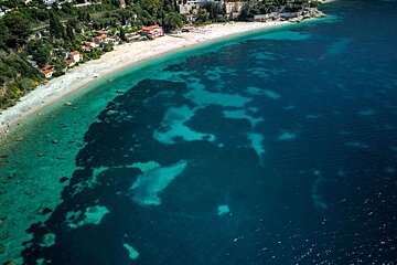 Aerial view of a beautiful coastal town with a sandy beach and vibrant turquoise sea. Underwater features are visible in the clear water.