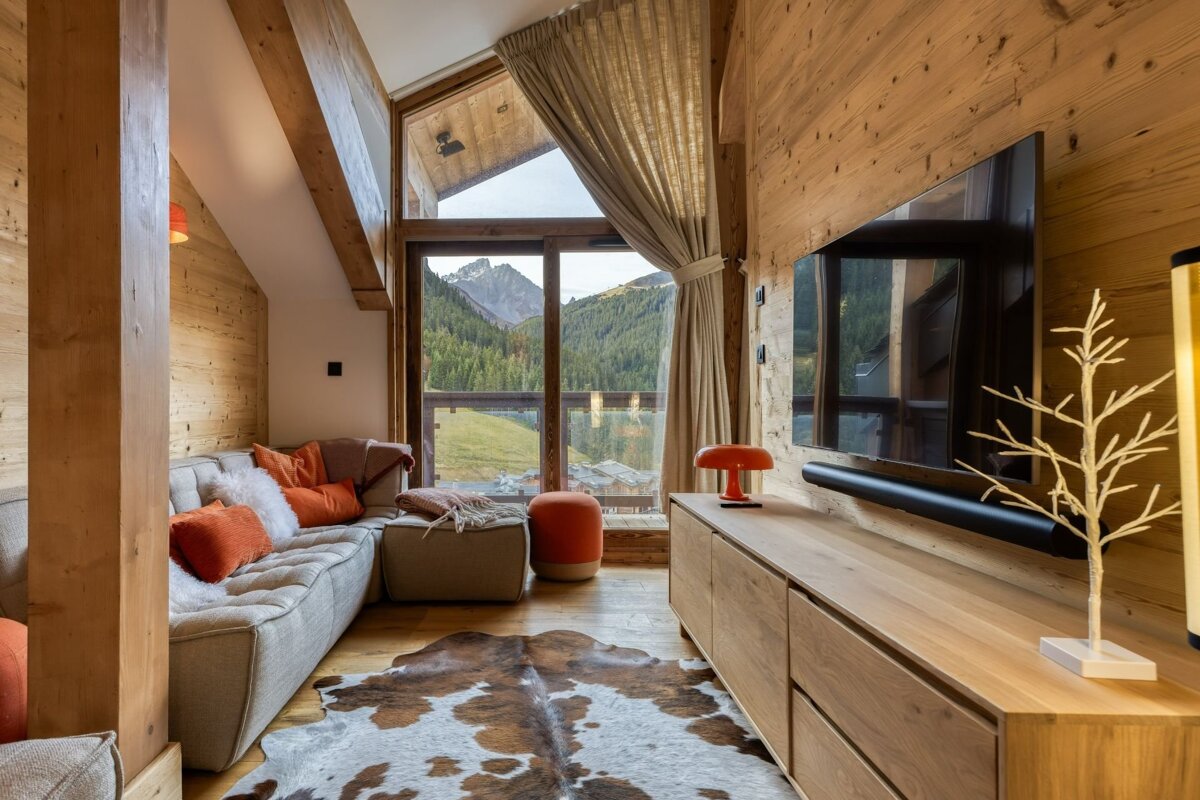 Cozy, modern, wood-paneled living room with large window showcasing stunning mountain views, complete with a comfortable sofa and cowhide rug.
