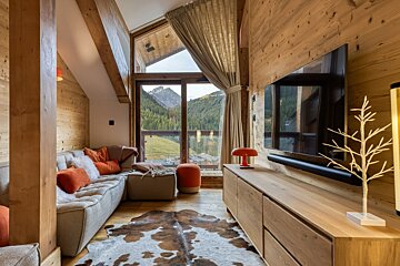 Cozy, modern, wood-paneled living room with large window showcasing stunning mountain views, complete with a comfortable sofa and cowhide rug.