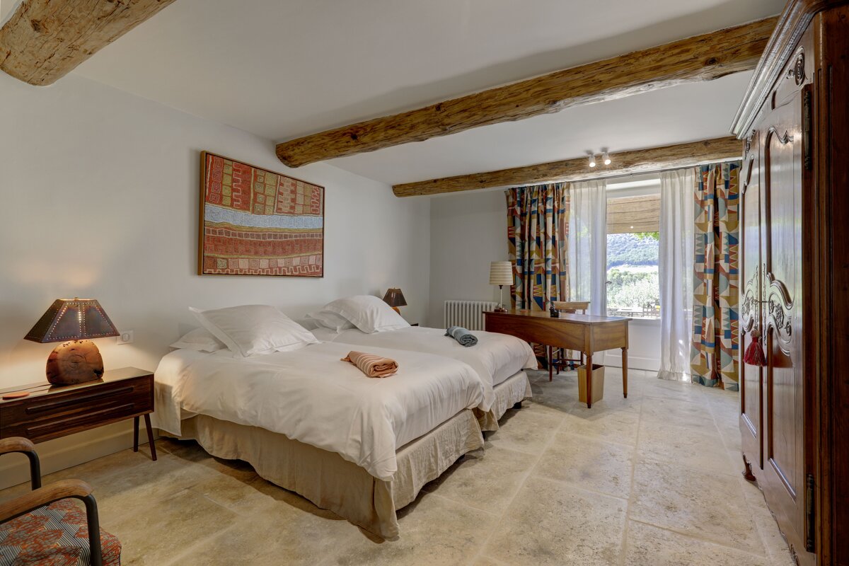 A bedroom with two beds a desk and a painting on the wall