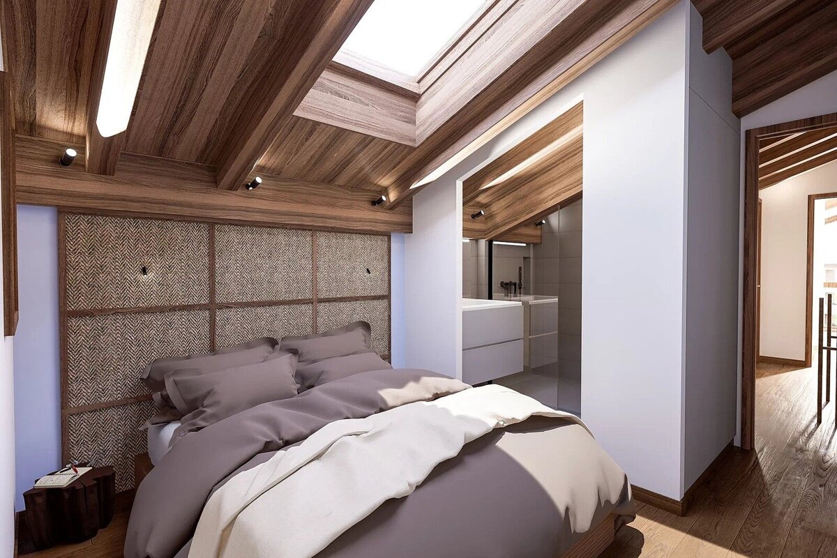 A modern attic bedroom features a wood-paneled vaulted ceiling with a skylight, a bed with neutral bedding, a woven headboard, and an open en-suite vanity.
