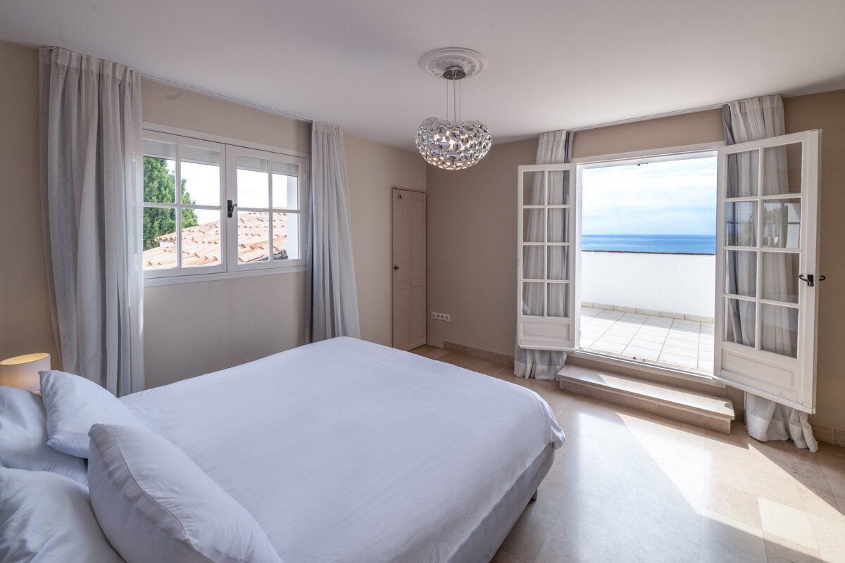 A bedroom with a large bed and a balcony overlooking the ocean