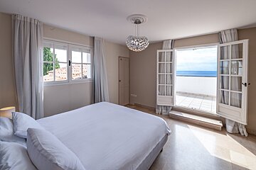 A bedroom with a large bed and a balcony overlooking the ocean