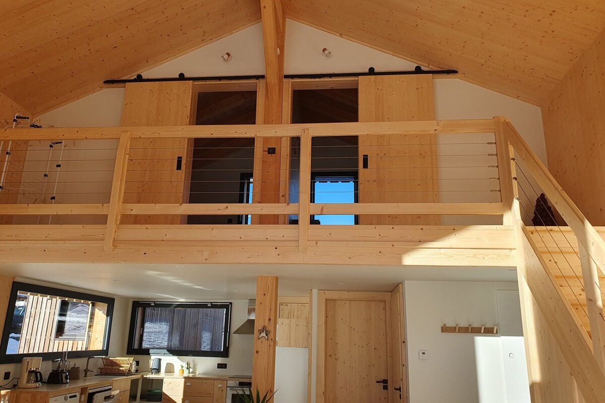 Bright, modern A-frame interior with natural wood walls, a loft, cable railing, and a kitchen below. Features sliding barn doors.