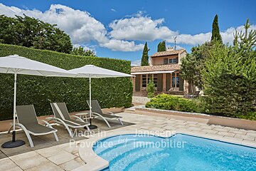 A swimming pool with chairs and umbrellas in front of a house that says made in provence by immobilier