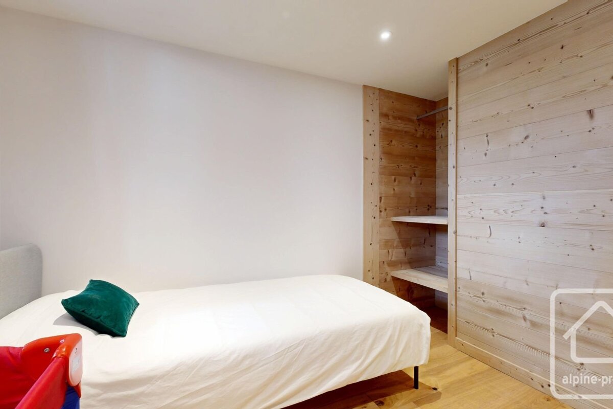 A simple bedroom with a single bed, white bedding, and a light-wood panel wardrobe area.
