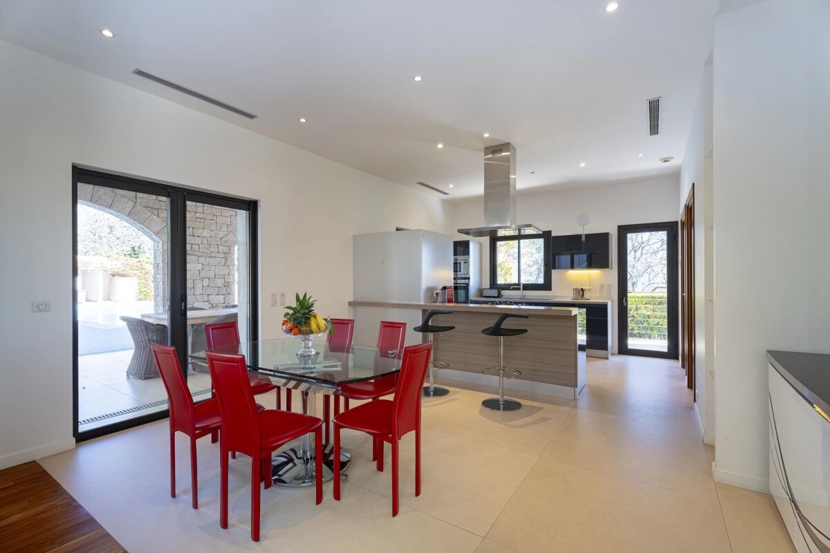 Bright, modern kitchen and dining area with vibrant red chairs, a glass table, and an island with bar stools. Patio access is visible.