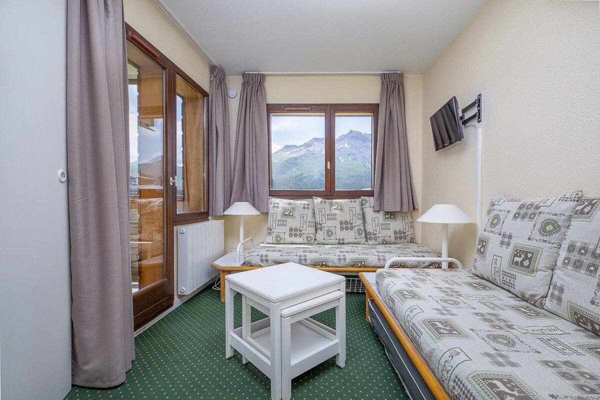Cozy bedroom with two patterned daybeds, green carpet, wall-mounted TV, and a window framing a beautiful mountain landscape.