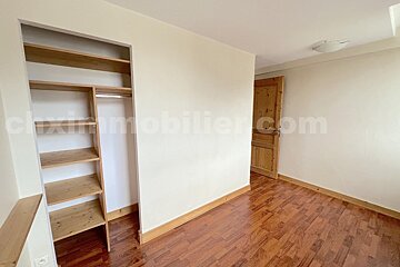 An empty room with light walls, a wooden floor, a built-in wooden closet with shelves, and a wooden door.