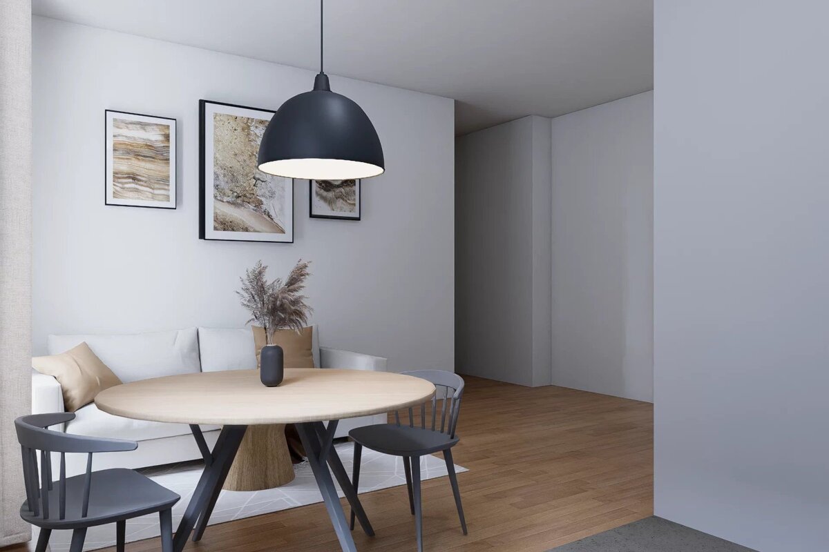 A modern, minimalist dining and living space featuring a round wooden table, dark chairs, white sofa, abstract wall art, and a black pendant lamp.