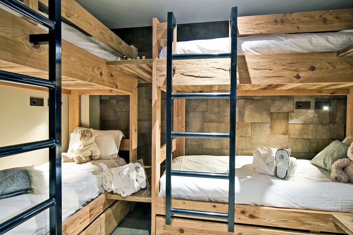 Rustic wooden bunk beds with black metal ladders, white bedding, and plush teddy bears.