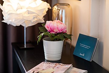 A white vase with a pink flower in it sits on a table