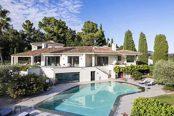 Luxurious white villa with terracotta roof, outdoor pool, and lush green surroundings on a sunny day.